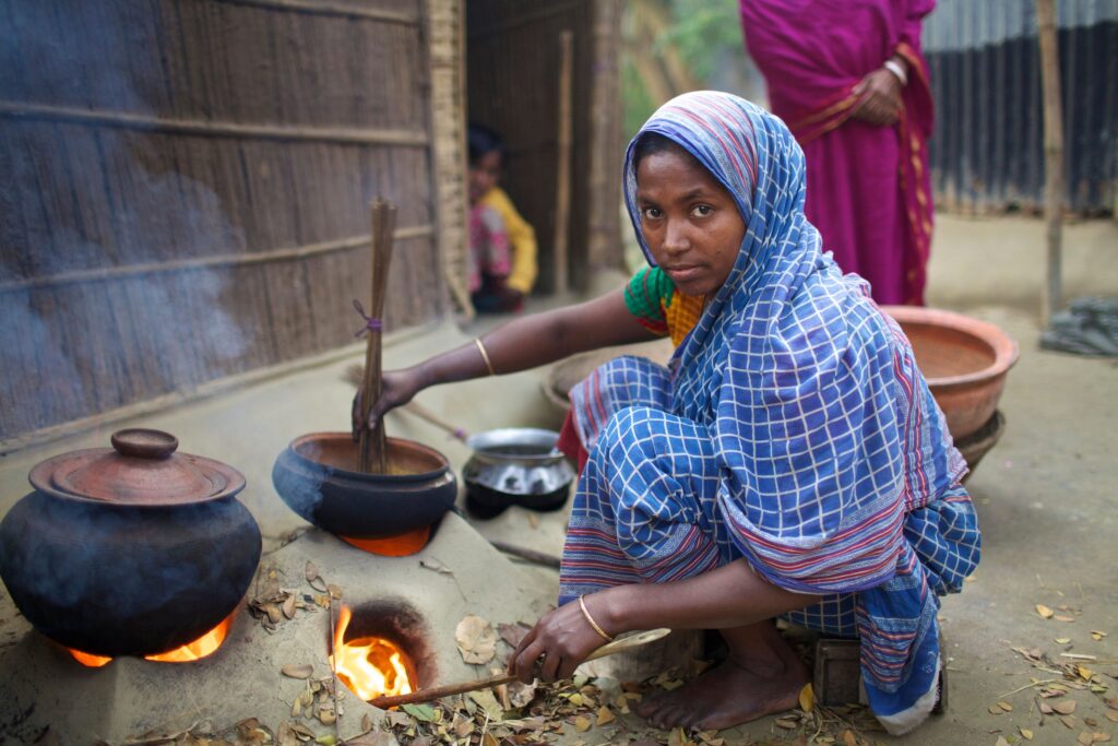 pexels photo 37560294 37560294 A woman in a blue sari uses a clay stove outdoors in rural Bangladesh, symbolizing traditional cooking methods.